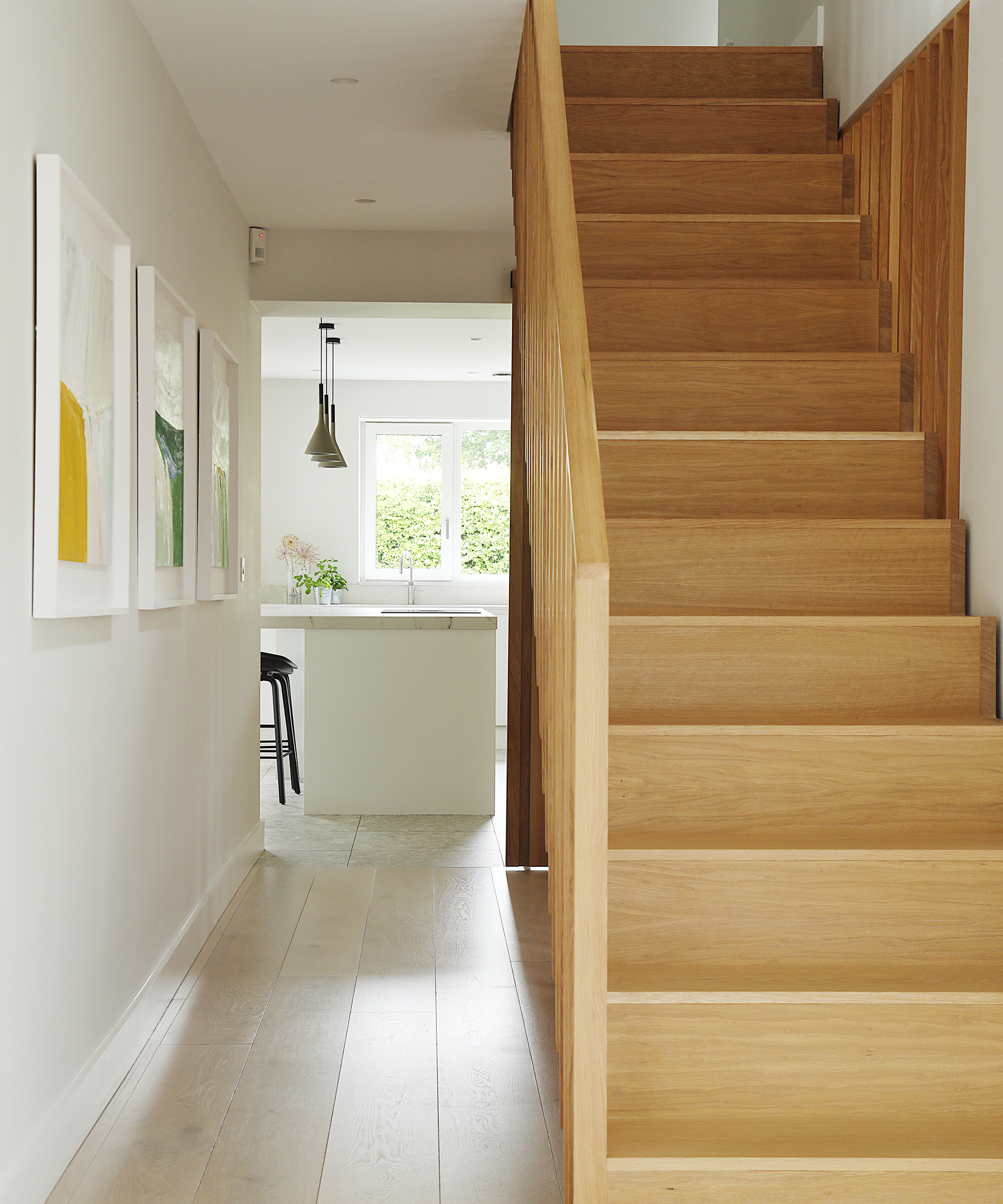 A wooden staircase leading up from a hallway with a kitchen in the background