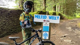 A young mountain biker by a blue graded trail sign