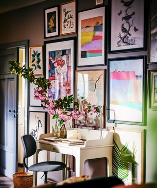small white desk placed with large bunch of flowers placed in front of a gallery wall with brightly coloured artwork