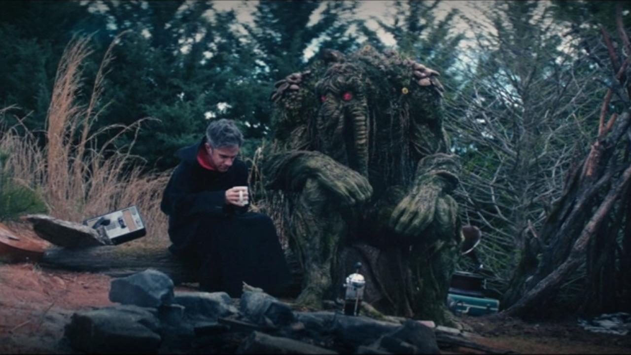 Man-Thing sits next to Jack Russell on a log next to a campfire in Werewolf by Night