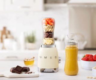 Smeg personal blender in cream on a countertop with a smoothie bottle beside it