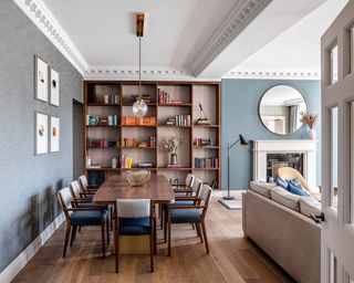 An open plan living and dining room with large walnut bookshelves and white fireplace
