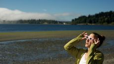 A woman wears eclipse glasses while standing on a beach