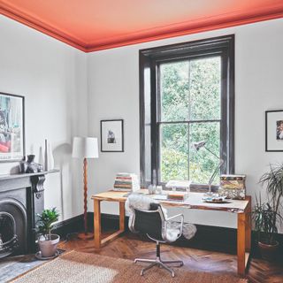 A home office with a coral-painted ceiling and silver desk lamp, as well as a wooden floor lamp