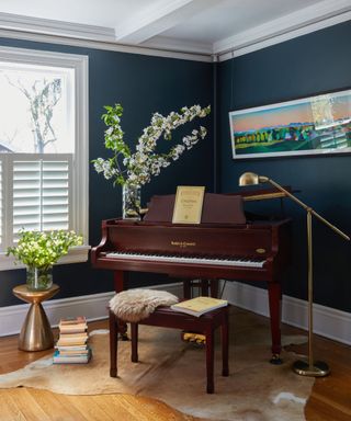 A blue living room with white shutters, a brown piano, and plants