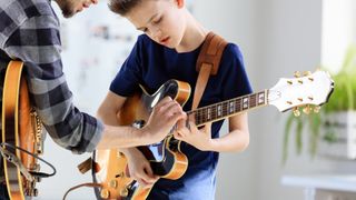 Boy gets shown how to play something on the guitar by another person