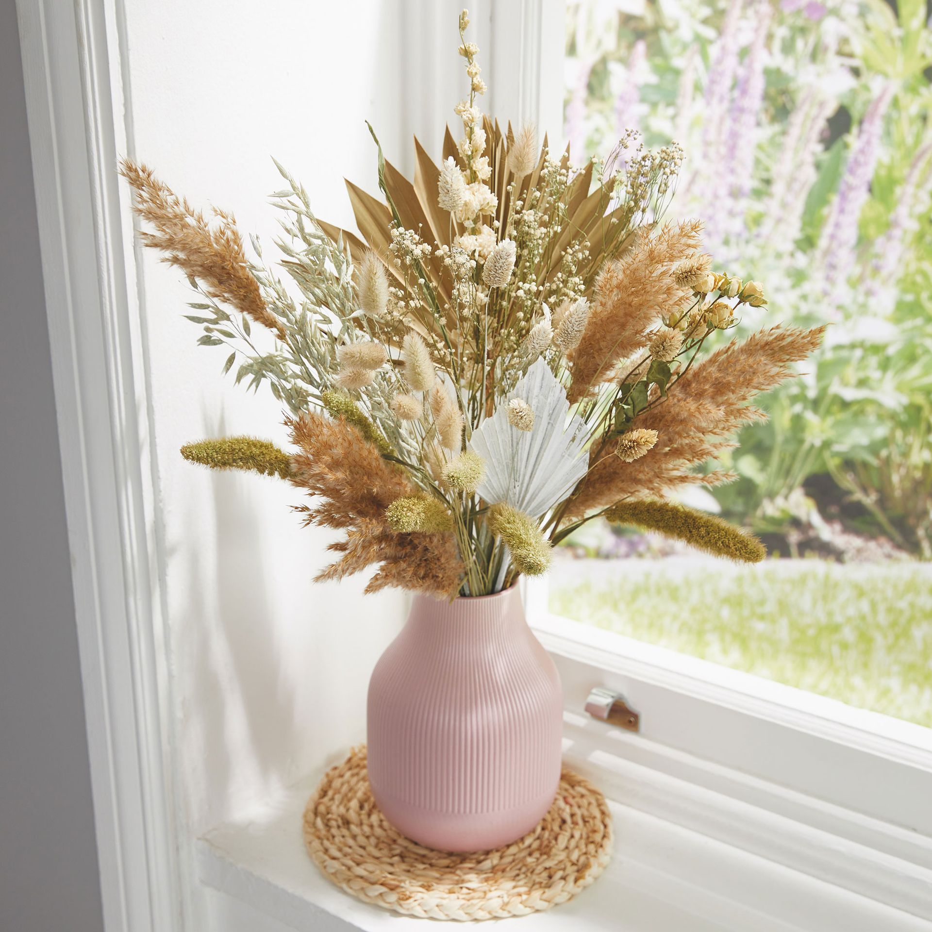 Bunch of dried flowers in ceramic vase on windowsill