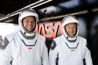 NASA astronauts Bob Behnken (at left) and Doug Hurley wear SpaceX spacesuits embroidered with and stand before NASA's "worm" logo atop the fixed service structure at Kennedy Space Center's Launch Complex 39A in Florida.