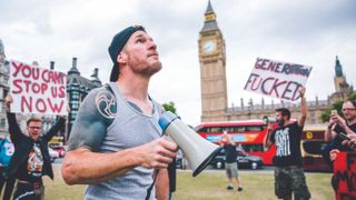 A photo of Tim Commerford and Wakrat outside the Houses of Parliament with signs and placards