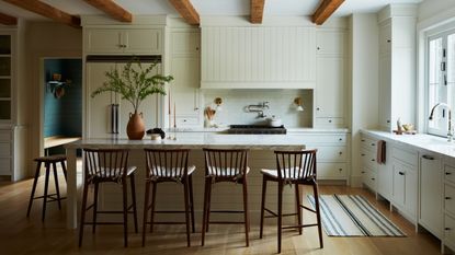 cream beamed kitchen with Shaker style cream cabinets, cream island and wooden bar stools 