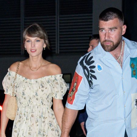 Taylor Swift wears a floral off-the-shoulder dress and holds hands with her husband Travis Kelce who wears a striped shirt