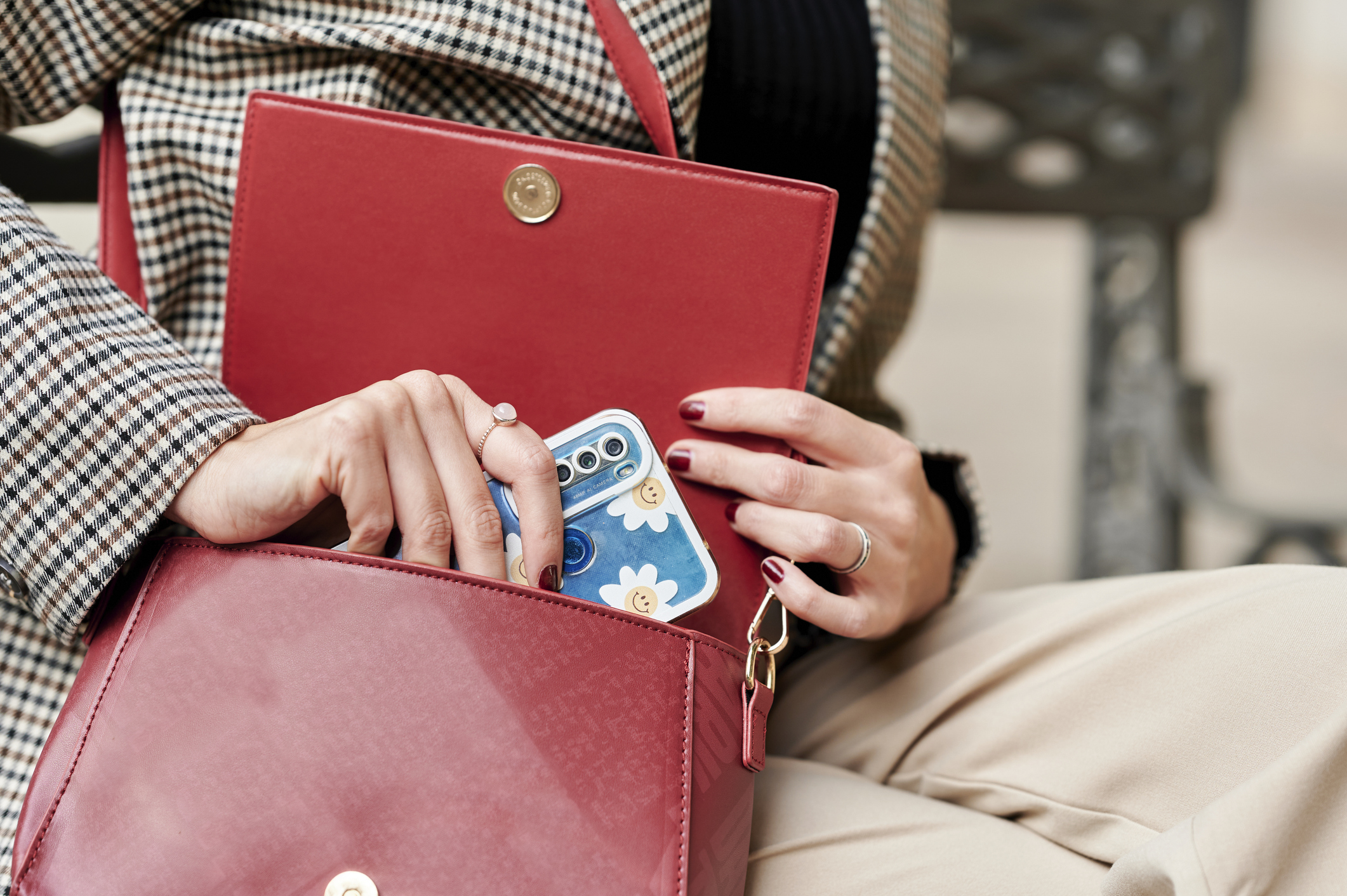 A close up of a person getting their phone out of their red handbag, wearing a grey, patterned blazer.
