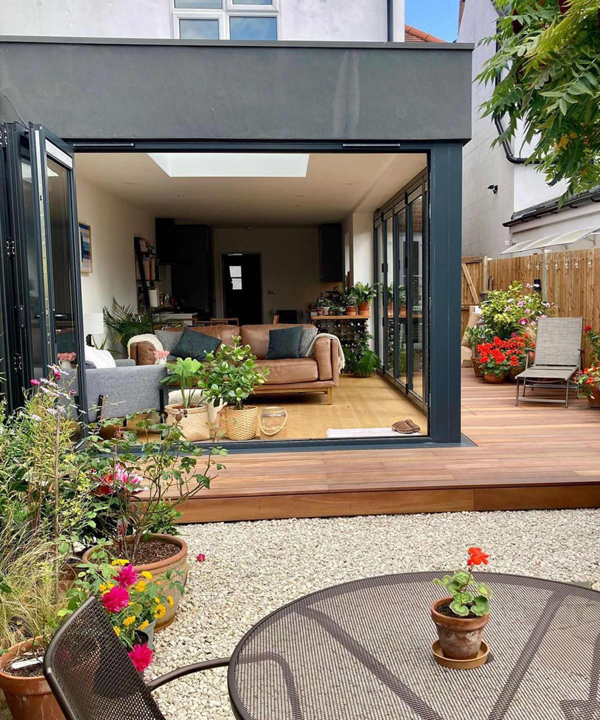 Edwardian garden with decking and bifold doors, brown sofa and outdoor garden chairs and tables with stone gravel on ground