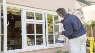 Man painting windows outside house