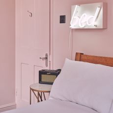 A pink colour-drenched bedroom with tonal bed linen and a neon light above the bed