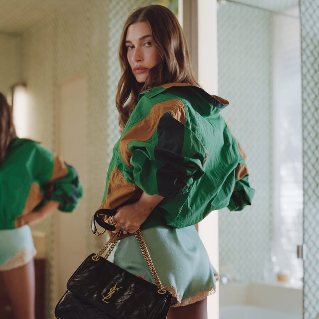 stand collar jacket trend 2026: Hailey Bieber. The model wears the stand collar jacket trend in the sold out green Saint Laurent motif. She styles it with satin lace trim short and a mid sized bag.