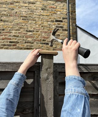 A person using a hammer to fix fence posts caps with house in background