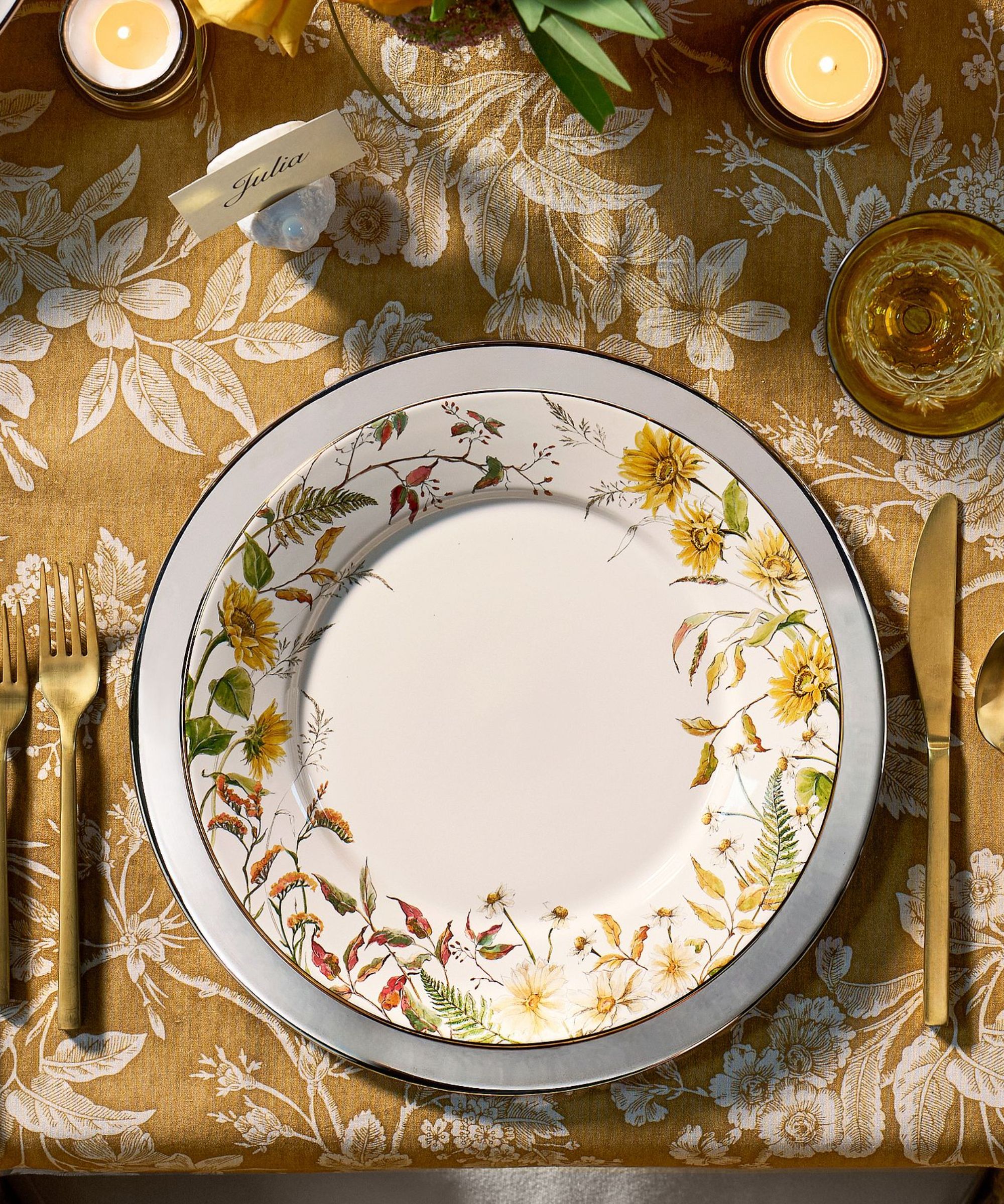 Table with yellow and white floral tablecloth, white plates with yellow flower motifs, and gold cutlery