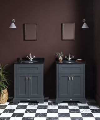 A bathroom with deep burgundy walls, two black vanity units with silver hardware, and a black and white marble checkerboard floor