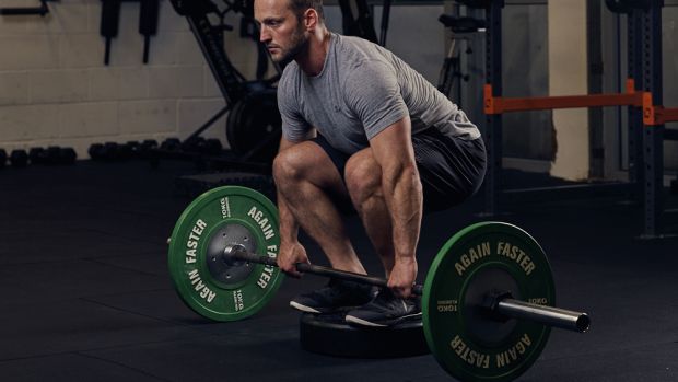 Man standing on weight plate about to perform deficit deadlift