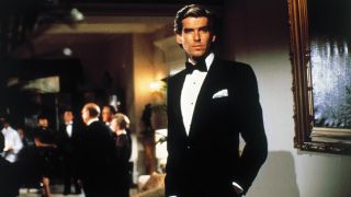 Pierce Brosnan stands dressed in a tuxedo while attending a party in Noble House.