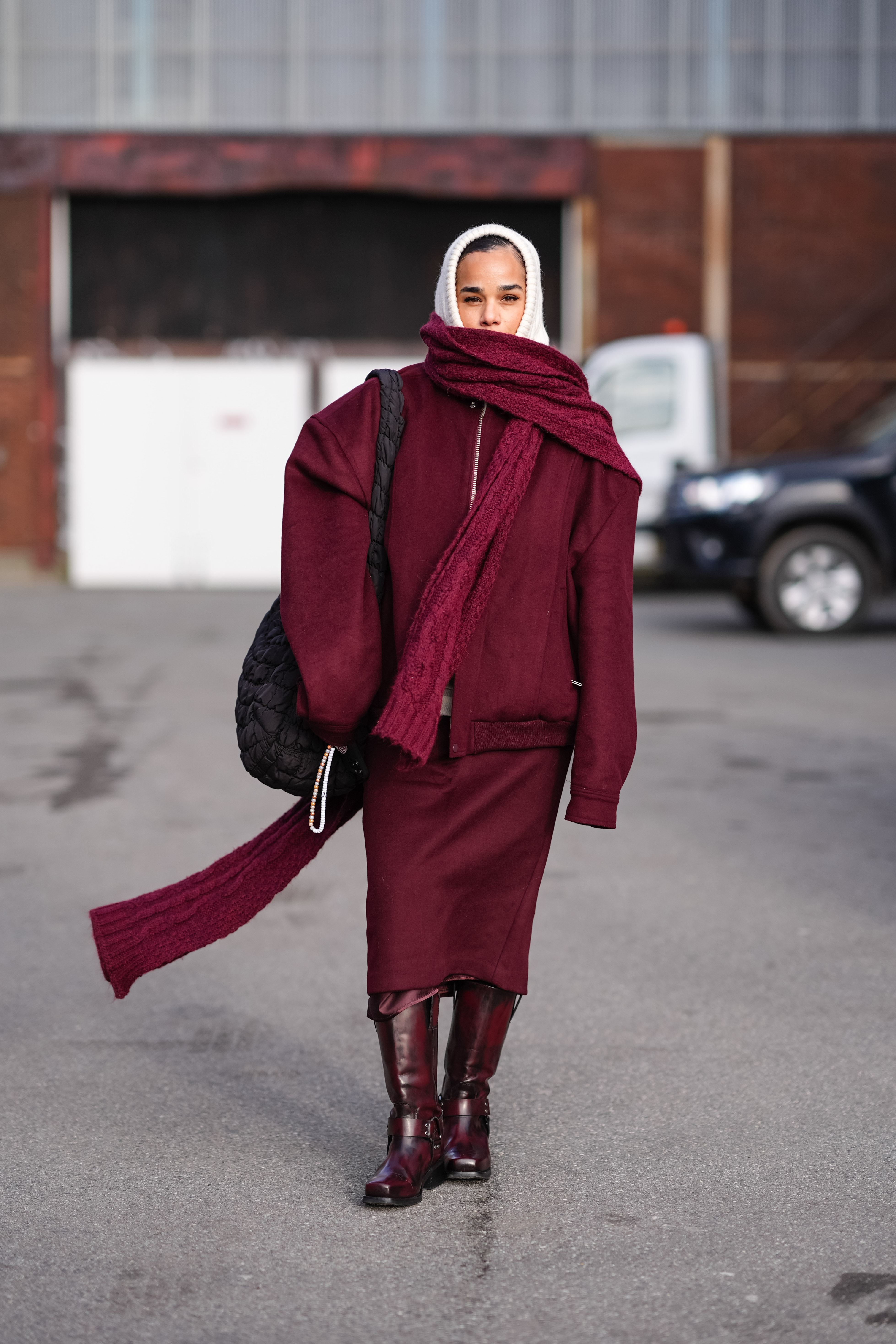 A woman wearing a burgundy jacket, skirt, scarf, and boots in street style
