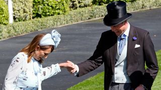 Prince William, Prince of Wales assists Carole Middleton as she gets the heel of her shoe stuck in the grass on day two of Royal Ascot 2024