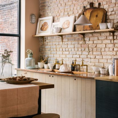 rustic kitchen with wood cabinets, copper worktop, brass taps, exposed brick wall, open shelf with artwork, artisanal tableware 
