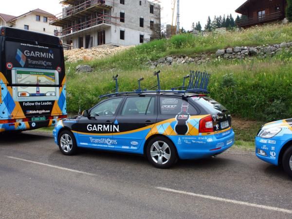 Team cars are lined up behind the bus in the designated parking area after the finish.