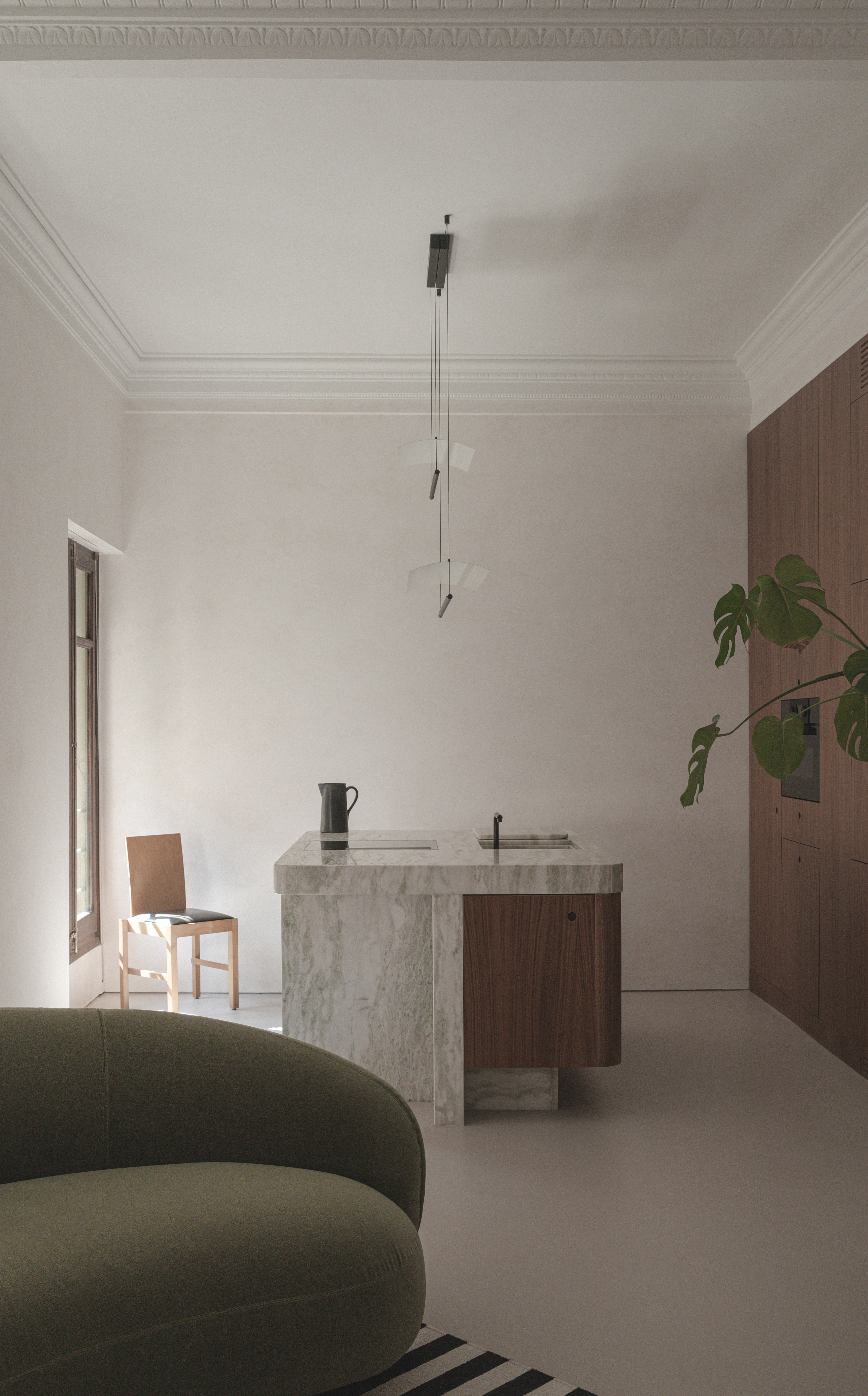 A minimalist kitchen in marble, with wood details, and a curving sofa in olive green placed close to it