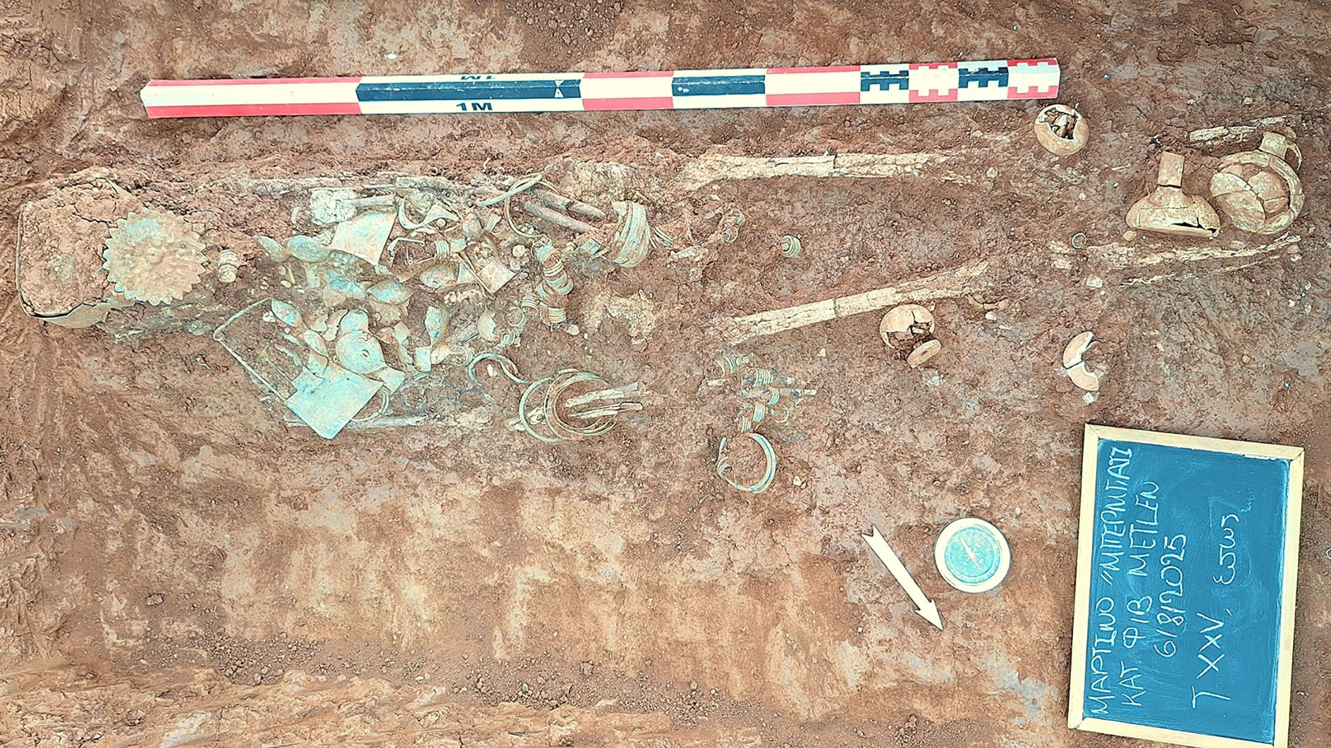 a human skeleton partially excavated with greenish bronze artifacts scattered around