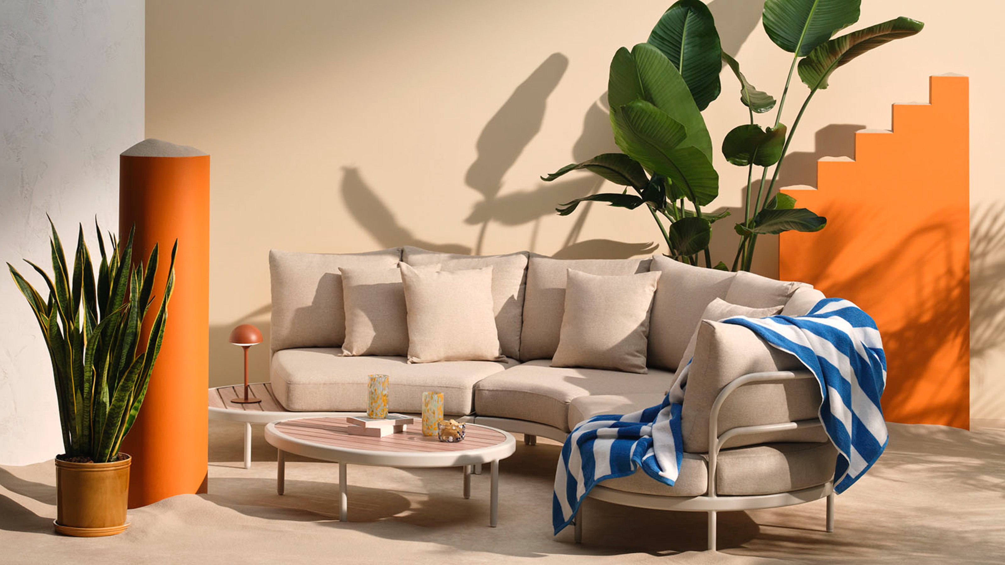 John Lewis Lozenge outdoor sofa with a coordinating coffee table and a striped towel on top on top of a sandy set