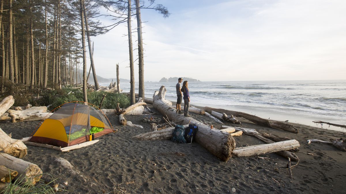 A couple on the beach looking out to see with a tent behind them