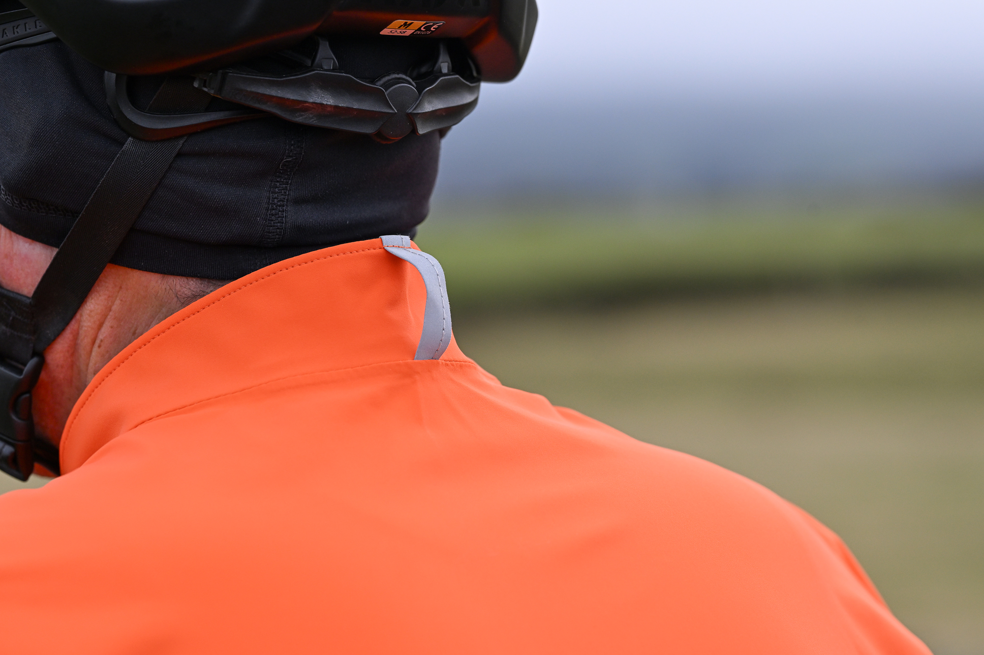 Close up of the rear of the collar on an orange jacket worn by a man wearing a black helmet