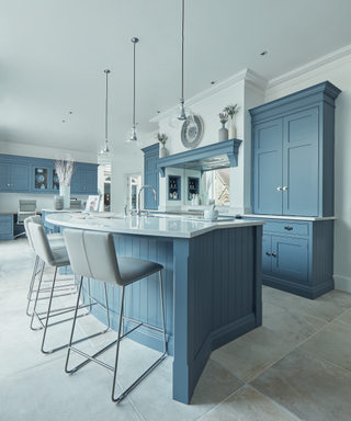 Curved breakfast bar ideas in a blue kitchen scheme with pendant lighting and travertine flooring.