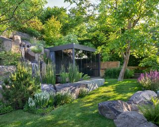 sloped garden with glass garden building surrounded by naturalistic planting and stone boulders