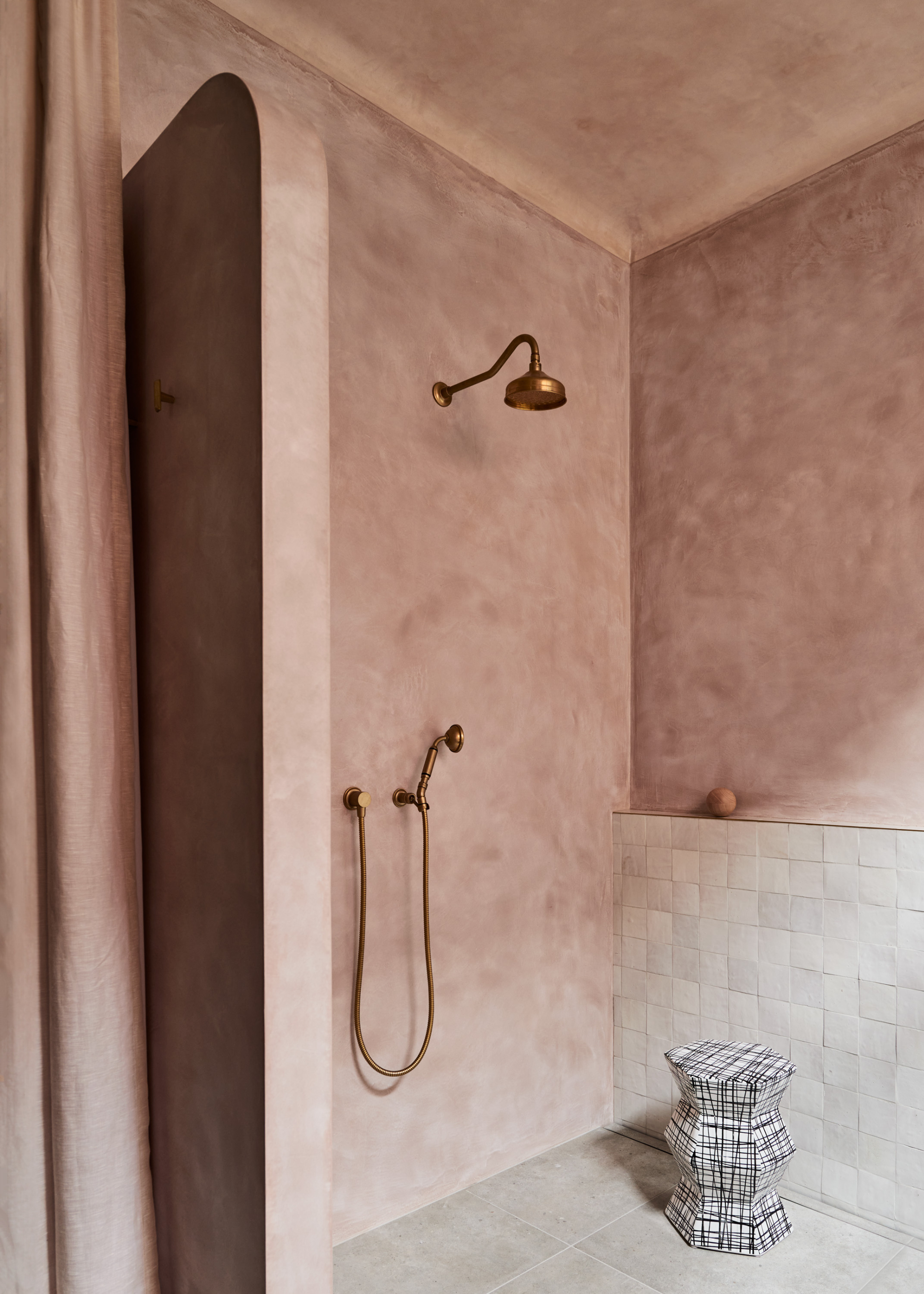 A shower room with limewash rose walls, a tiled accent wall, a stool, and brushed brassy gold hardware