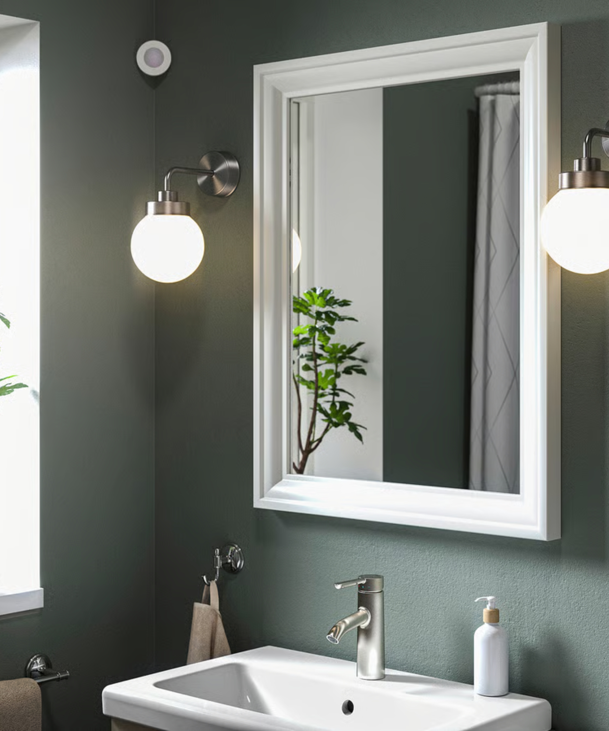 IKEA MYGGSPRAY smart motion sensor in dark bathroom above two bright wall lights, a mirror, and a bathroom sink.