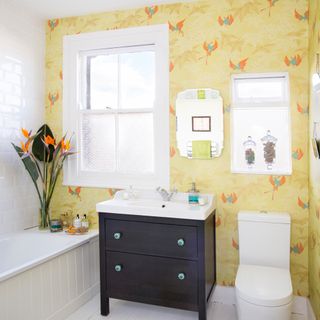 bathroom with yellow bird designed wallpaper white window commode and black drawer