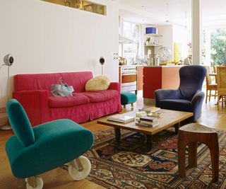 Open plan kitchen-diner with white walls, deep pink couch, green chair on wheels and wooden coffee table