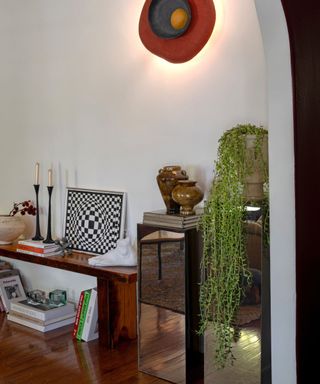 stylized corner of a living space with a wooden sofa, stacked books and various eclectic decor pieces