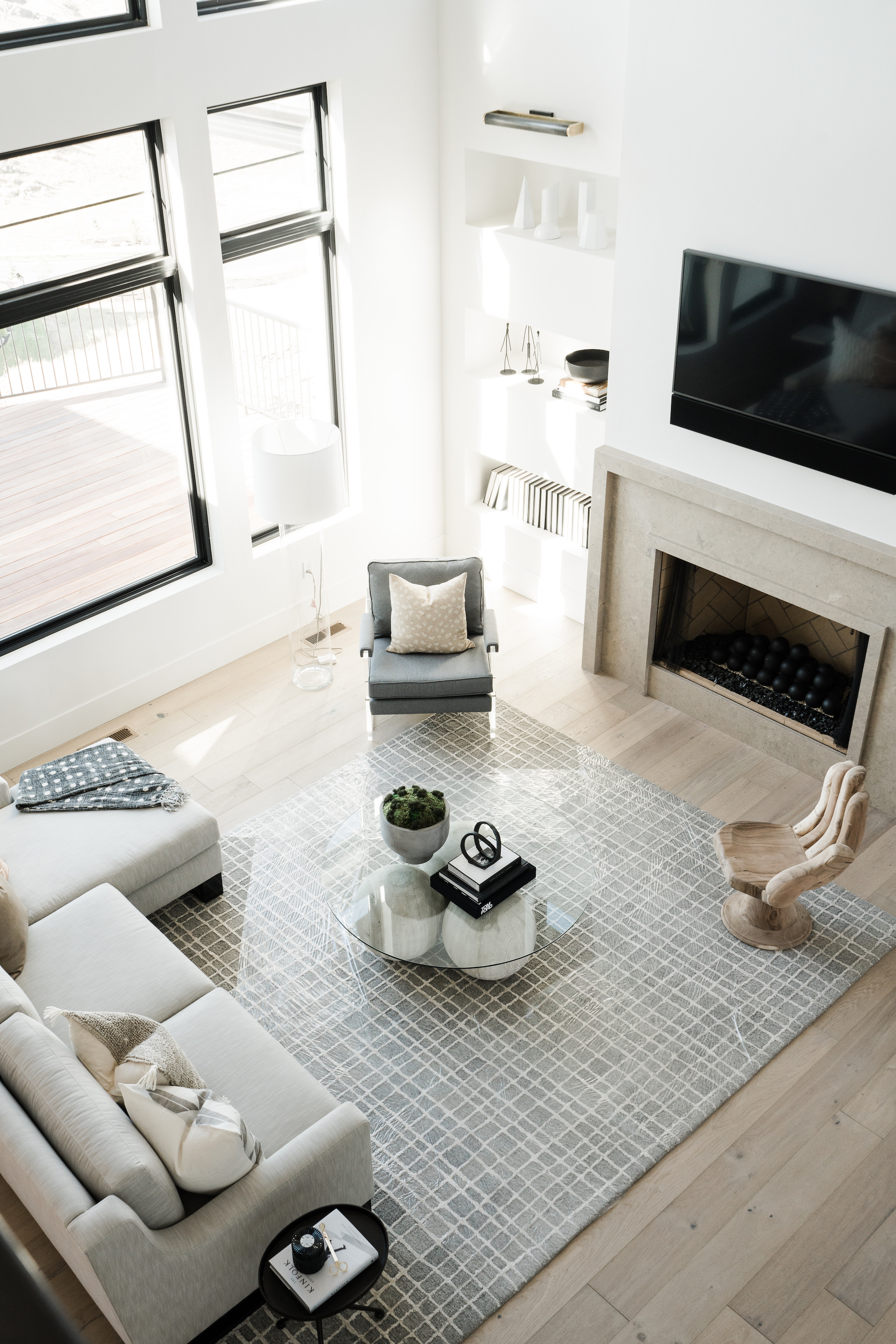 white living room with neutral furniture, glass coffee table, check rug, white shelving