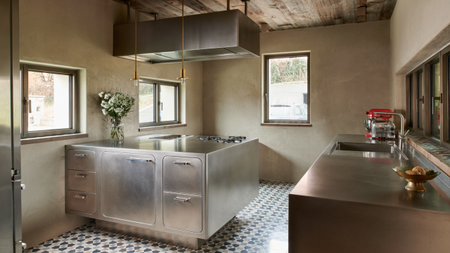 a beautiful stainless steel kitchen with gold detailing, ceramic tile floors, and neutral walls