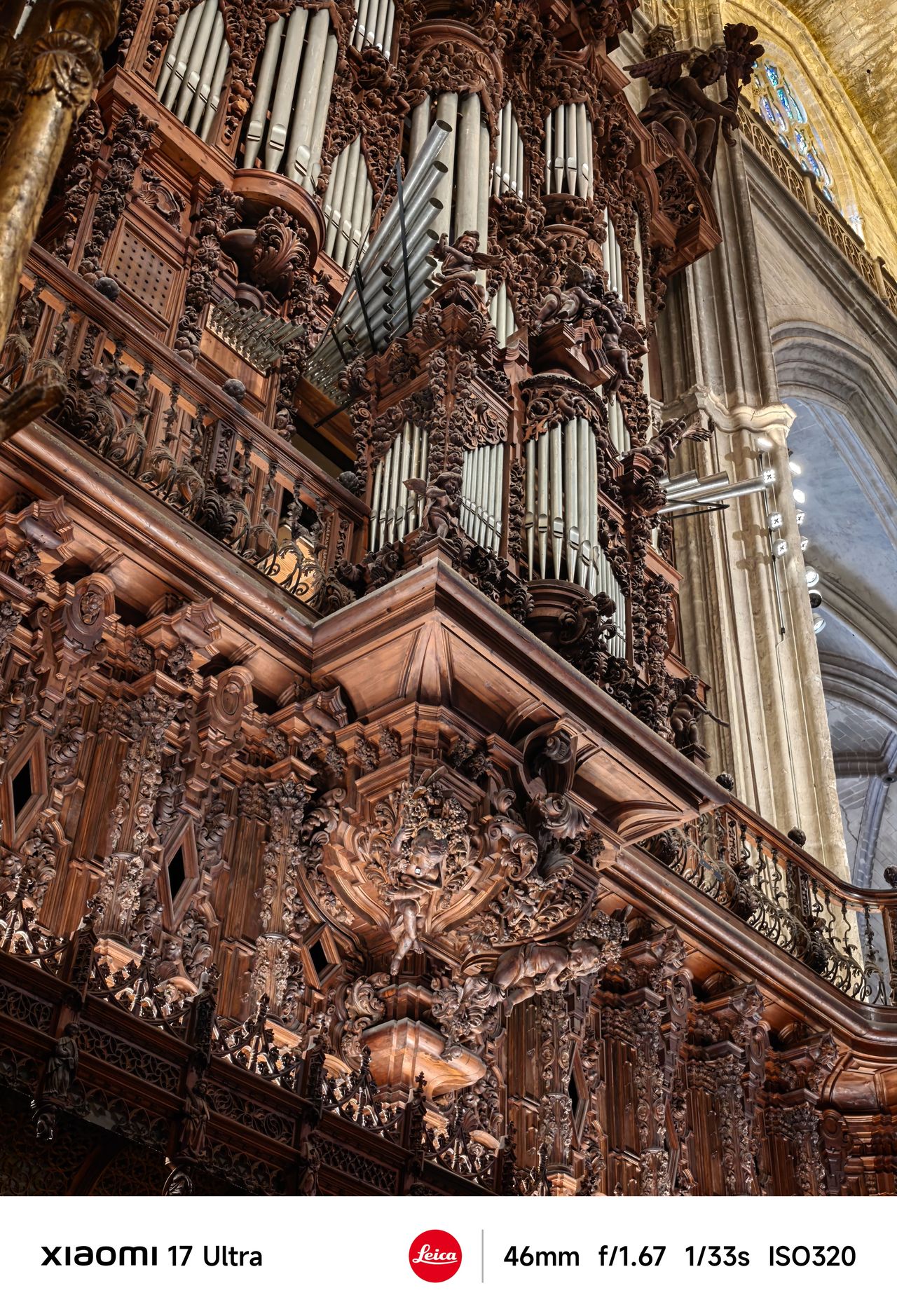 Intricately carved wooden pipe organ inside a cathedral, lit by warm interior light.
