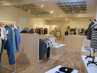 Tres Bien Shop, Sweden. A clothing store with clothing displayed on rails and mannequins with a wooden floor and a square skylight.
