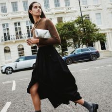 Woman crossing the street wearing black skirt and brown jumper