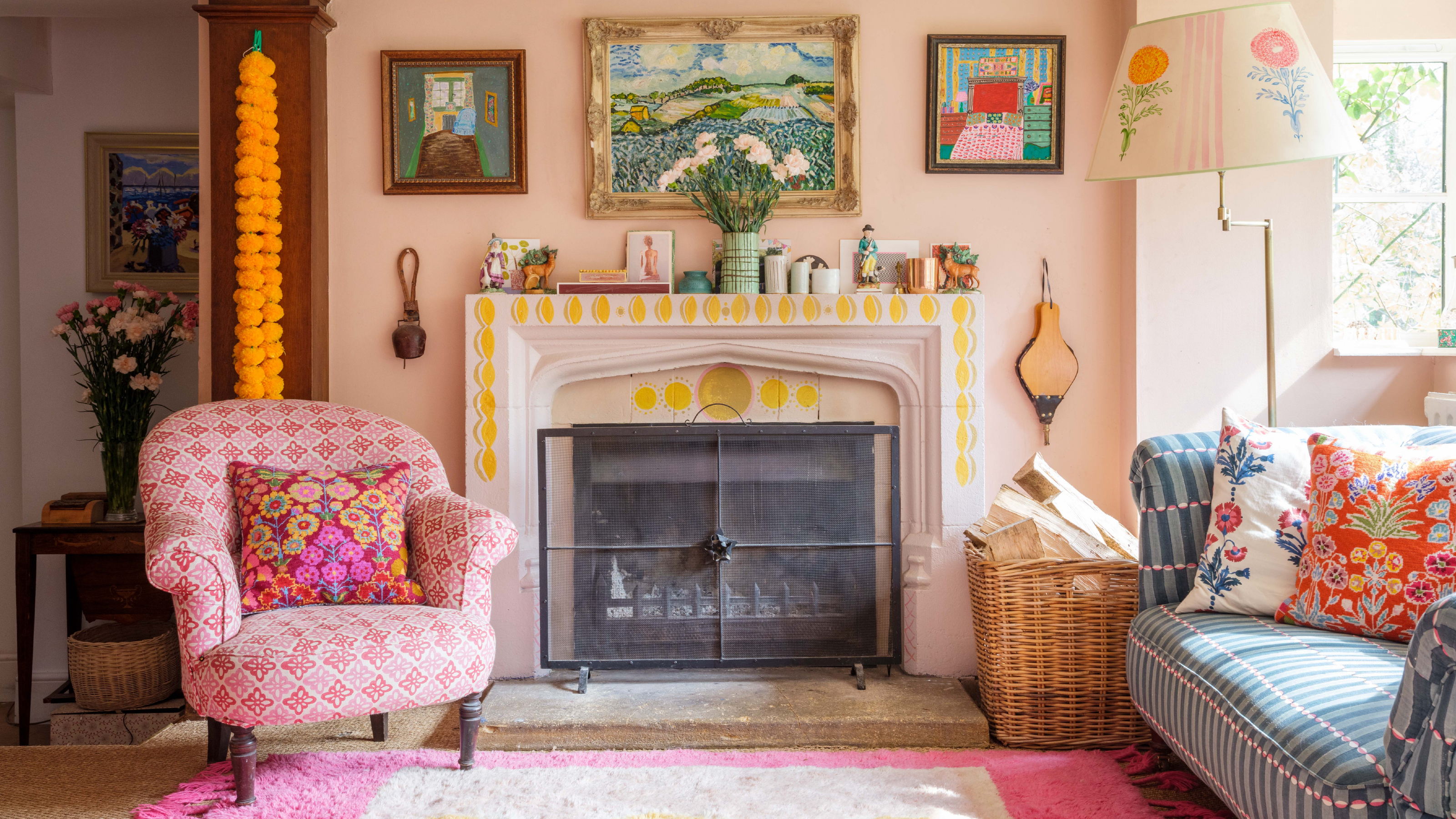 cottagecore living room ideas, colourful living room with decorated fireplace, pastel pink walls, rugs, blue print sofa, bright cushions, Charleston style prints, mix and match patterns