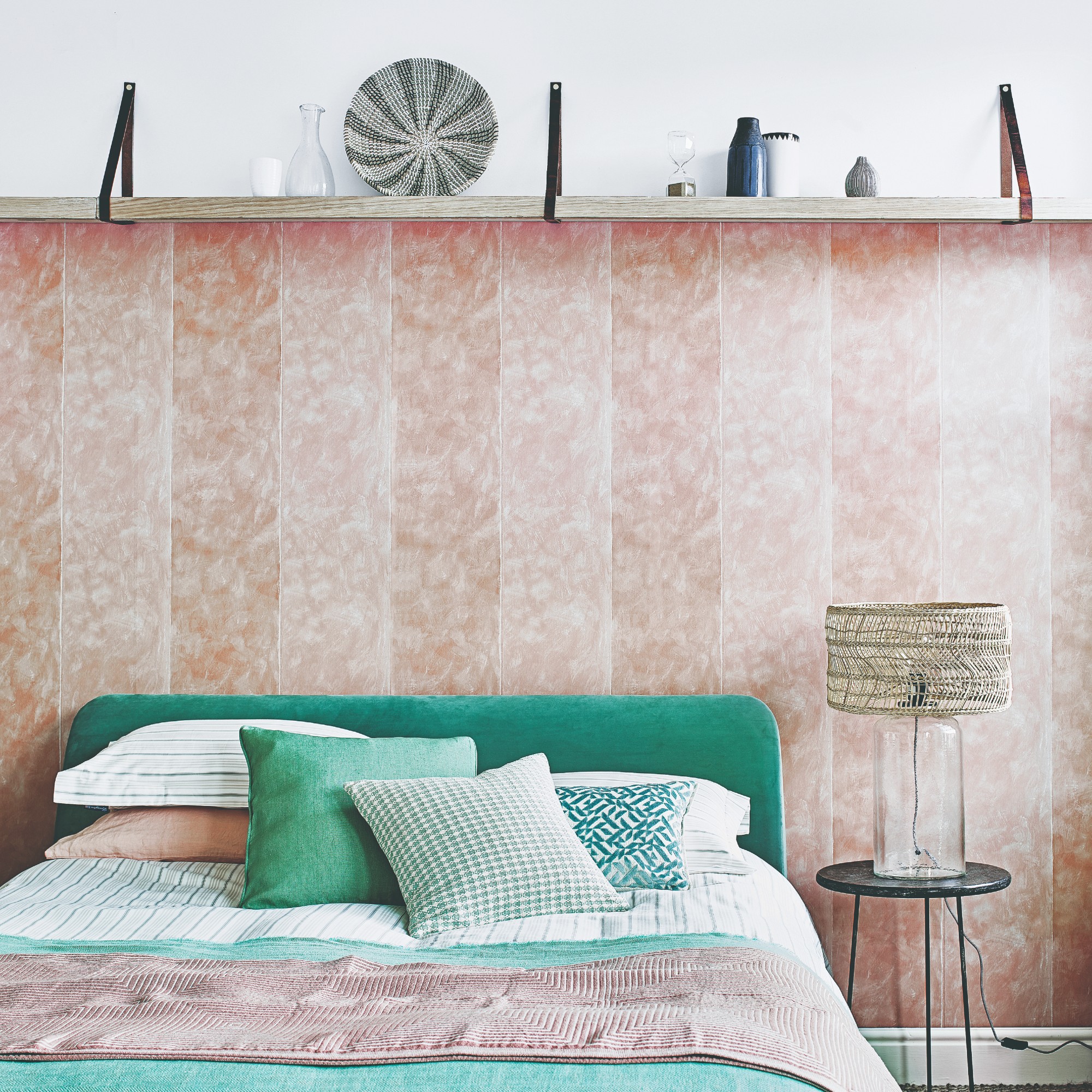 A bedroom with the feature wall behind the bed partly covered in a pink wallpaper stopping at a picture ledge