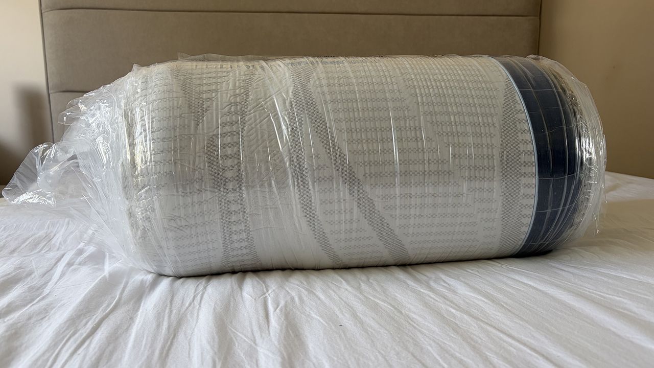 The DreamCloud Softer Mattress Topper wrapped in plastic on the bed of our mattress tester Ruth Jones
