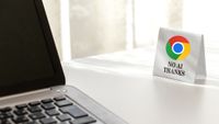 A laptop on a white desk faces a small sign with the Google Chrome logo, saying "No AI Thanks."